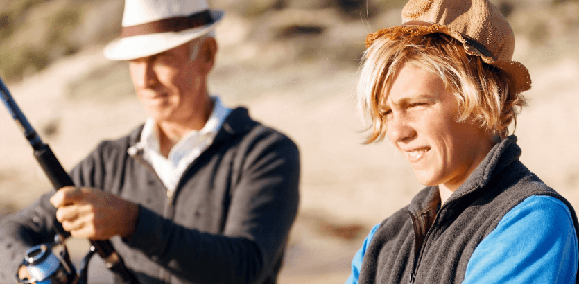 A man and a boy enjoy fishing together on a serene beach, surrounded by gentle waves and a clear sky.