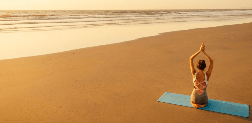 A woman practicing yoga on a serene beach, surrounded by gentle waves and a clear blue sky.