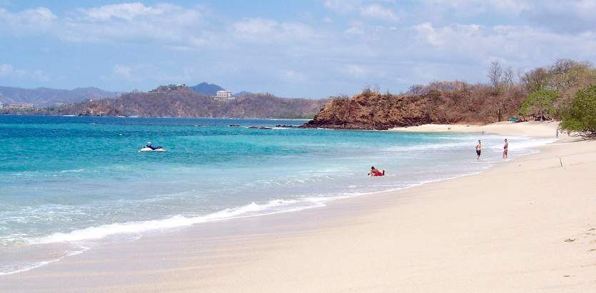 A sunny sandy beach filled with people enjoying the sun and surf, creating a lively and vibrant atmosphere.