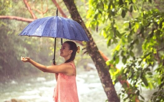 A woman stands in the rain, holding a colorful umbrella to shield herself from the downpour
