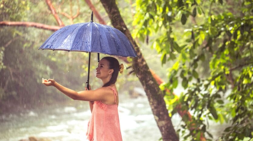 A woman stands in the rain, holding a colorful umbrella to shield herself from the downpour