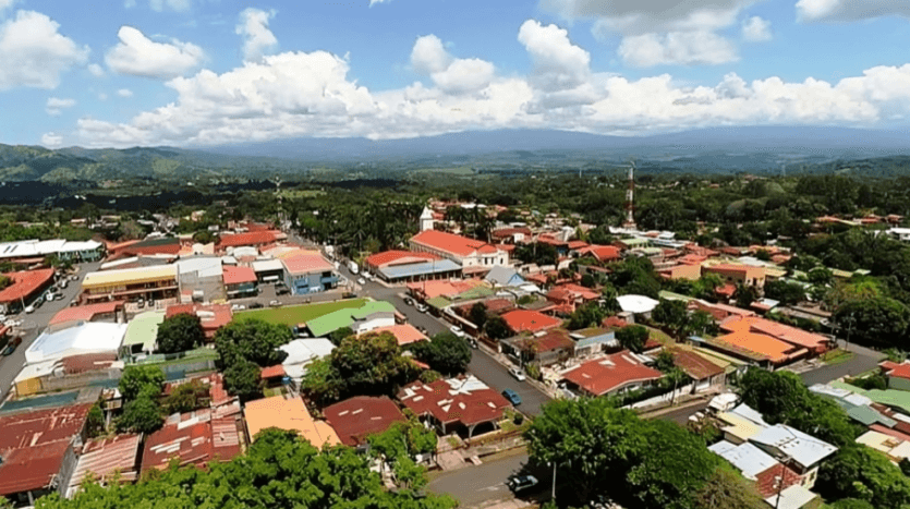 Aerial view of a town nestled below mountains, showcasing rooftops and natural scenery in the background.