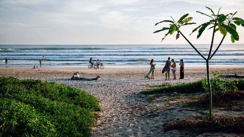 A group of people strolls along the sandy beach, with the ocean waves gently lapping at the shore.