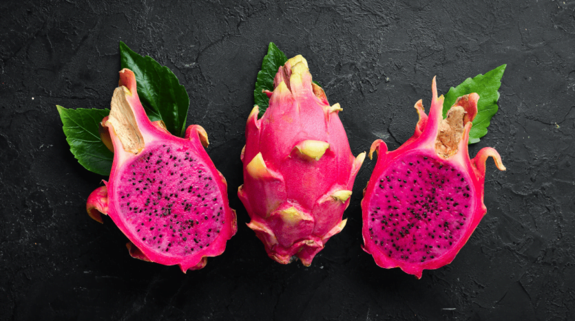 Three vibrant dragon fruits displayed against a sleek black background, showcasing their unique texture and color.