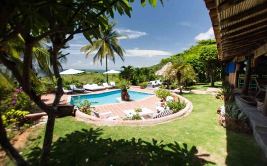 A serene tropical pool and lounge area surrounded by lush greenery and vibrant flowers, inviting relaxation and leisure.