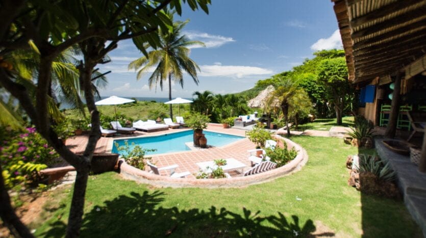 A serene tropical pool and lounge area surrounded by lush greenery and vibrant flowers, inviting relaxation and leisure.