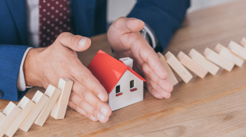 A businessman carefully holds dominoes, arranging them to construct a miniature house, symbolizing strategic planning and growth.