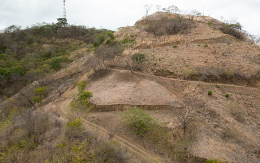 A dirt road winding upward, leading towards a hill under a clear blue sky.