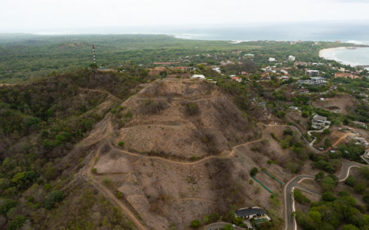 Aerial view of a hillside featuring a winding road and several houses nestled among the greenery.