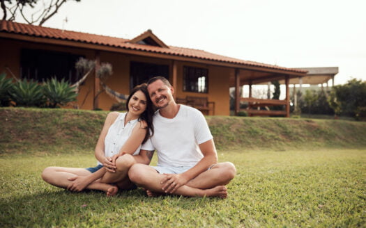 A man and woman seated on the grass, enjoying a moment together in front of a charming house.