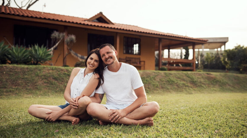 A man and woman seated on the grass, enjoying a moment together in front of a charming house.